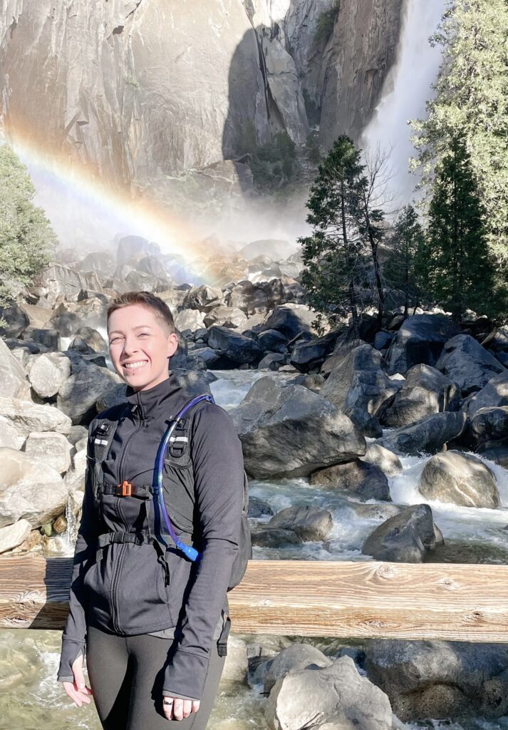 Woman standing in front of waterfall and rainbow