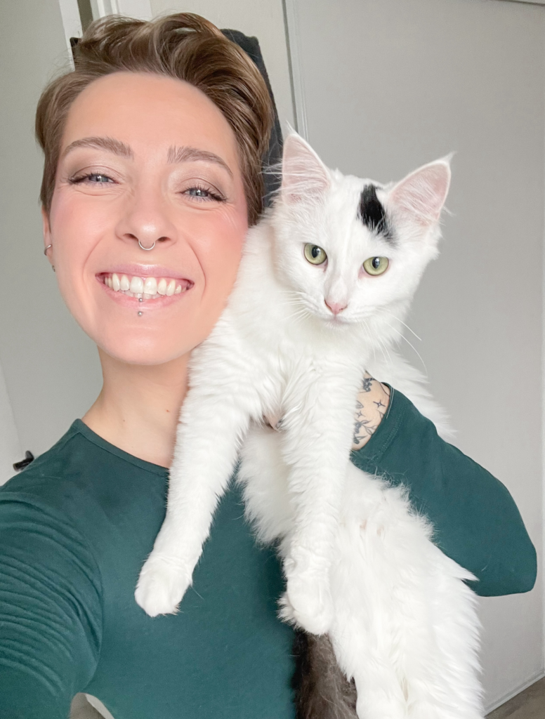 Woman holding her white cat up next to her and smiling