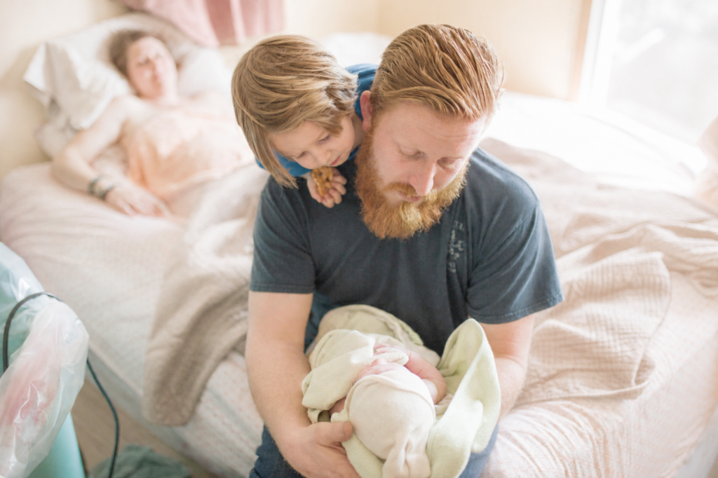 Man holding newborn baby born at home with toddler son on shoulders
